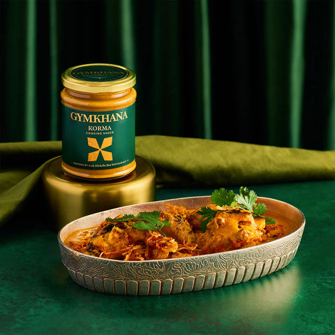 Jar of korma cooking sauce with a prepared dish on a green backgroud