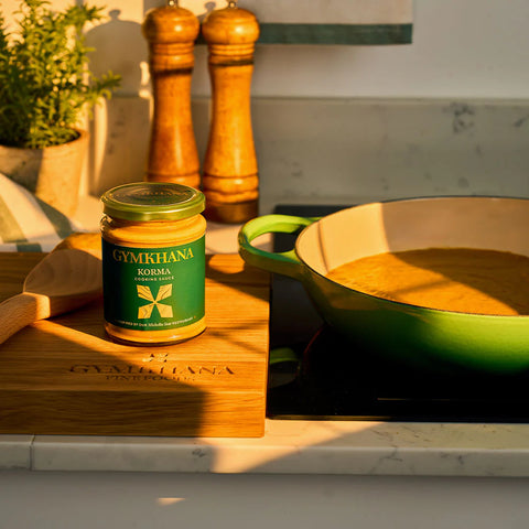 jar of korma cooking sauce on a wooden cutting board next to salt & pepper shakes and a green pan