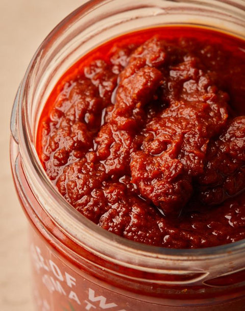 A close-up shot of a glass jar filled with chunky, dark red tomato paste or sauce, with the label partially visible at the bottom.