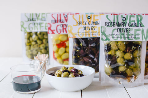 bags of different kinds of olives with a bowl of the rosemary garlic olives on a white surface