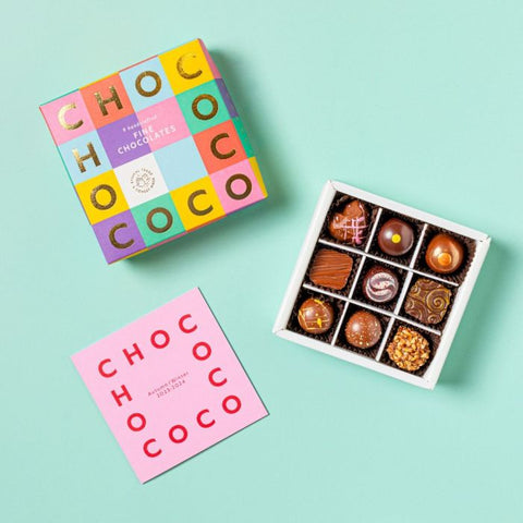 Colorful chocolate box with a pink card and open box of chocolates on a light blue background